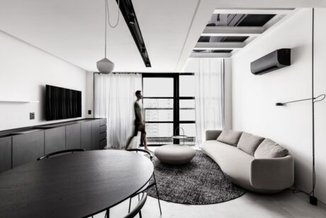 A man stands in the living room of a modern apartment, showcasing sleek design and minimalist decor in a stylish urban setting.