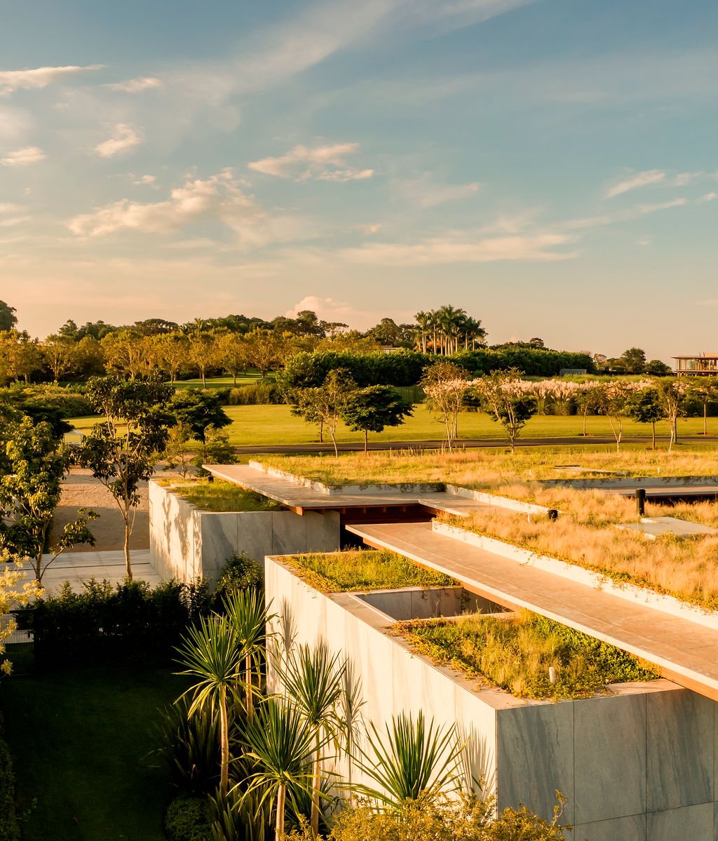 Planted green roof of Casa CLL by Bernardes Arquitetura seen at golden hour, with stone-clad blocks below and the open countryside of Porto Feliz beyond