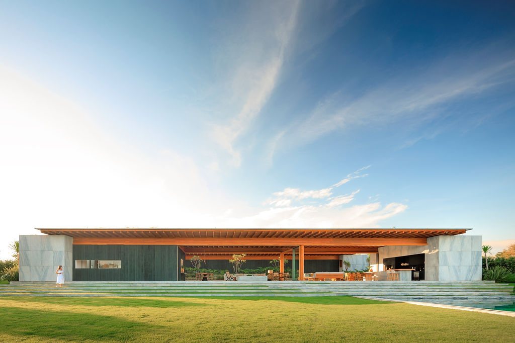 Full elevation of Casa CLL by Bernardes Arquitetura, a long horizontal house with stone blocks, charred timber walls and an open social area under a single roof