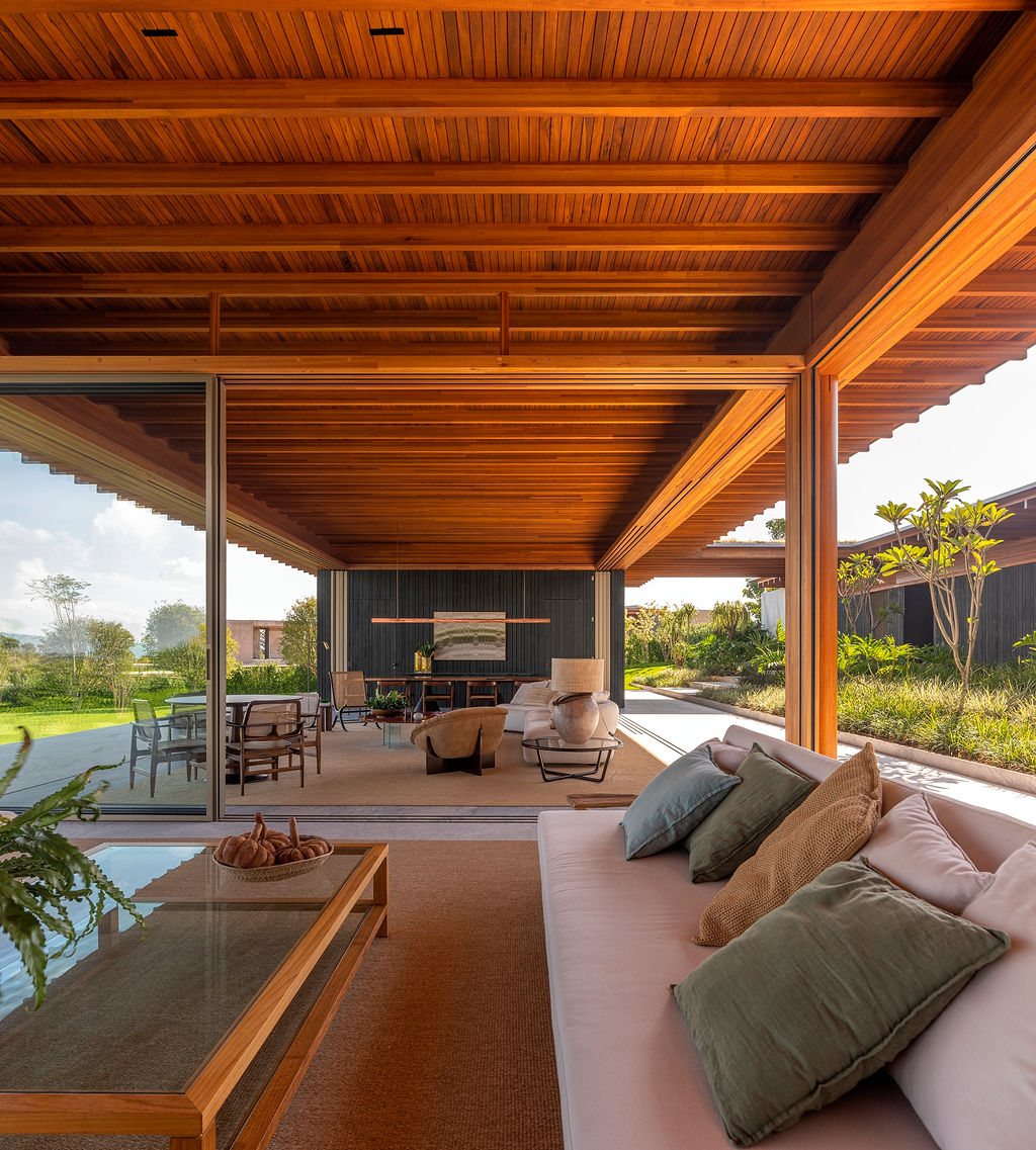Covered terrace at Casa CLL by Bernardes Arquitetura, with exposed timber ceiling, a low sofa and views to the garden and social areas in Porto Feliz, São Paulo