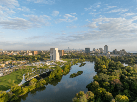 Aerial view of the Obama Presidential Center campus along Jackson Park in Chicago, featuring landscaped green spaces, a reflective lagoon, and the city skyline in the distance.