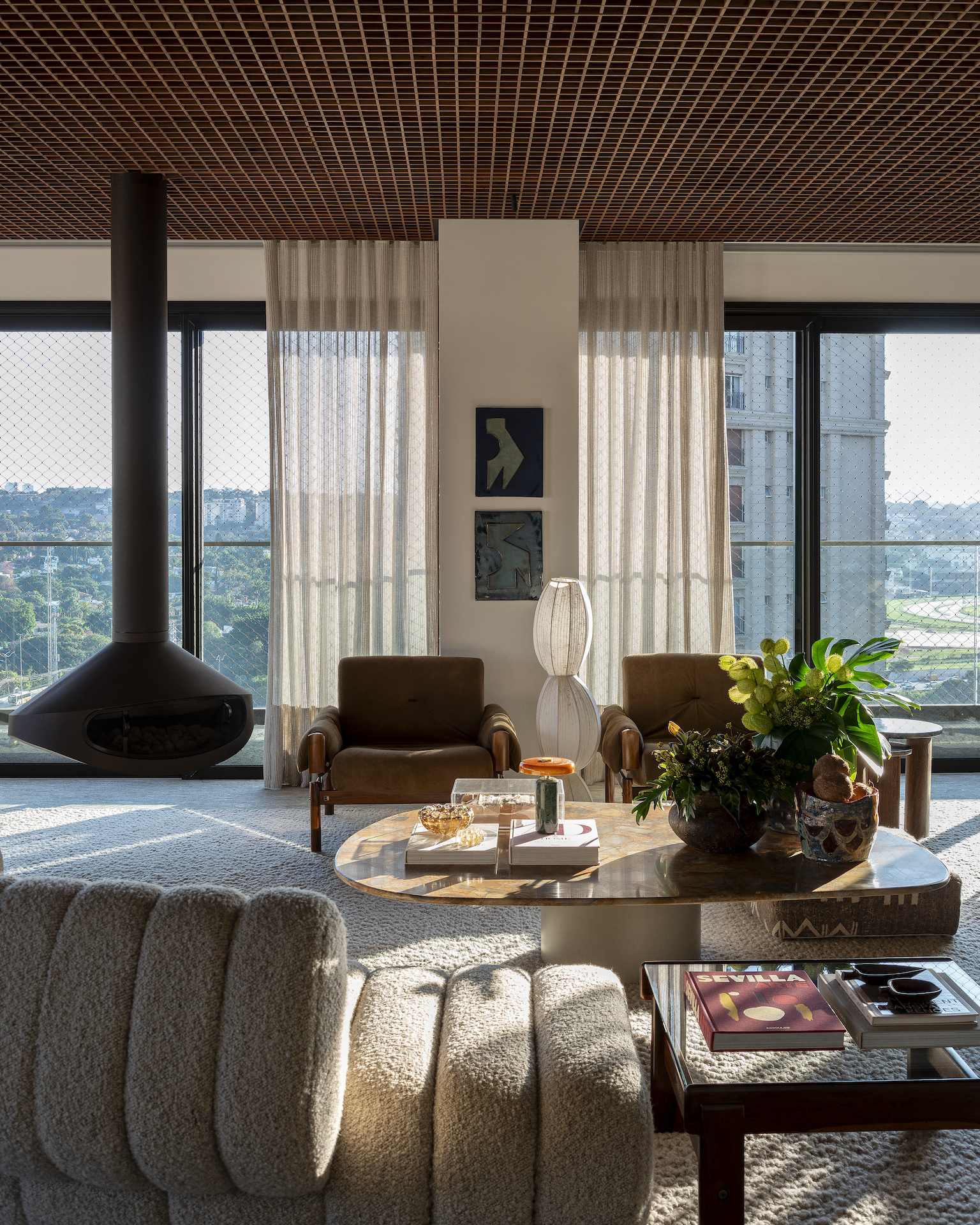 Seating detail at CRR | Arborea by Triplex Arquitetura, with brown leather armchairs, sculptural stone table, artworks and a suspended fireplace against the window