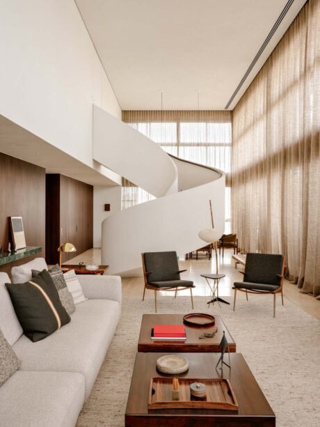 Autem Apartment by Felipe Hess Arquitetos in São Paulo, wide view of the double-height living room with the white helical staircase rising against tall sheer curtains and Nordic furniture
