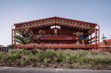Campus Betterware Guadalajara by Estudio MMX and Luis Campos in El Arenal, Jalisco, long red steel-and-concrete façade with cross-braced bays and glazing rising above dense green planting